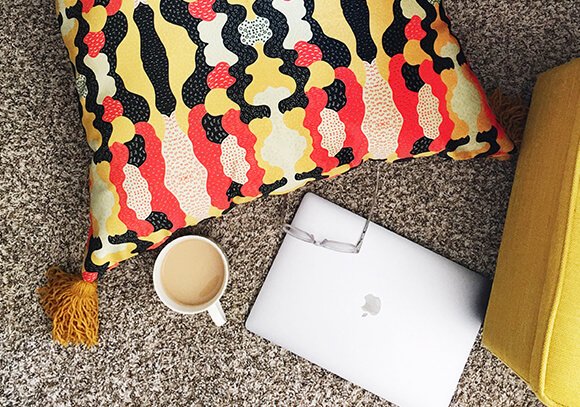 Floor Pillow in Celosia Velvet Overhead shot of a laptop, cup of coffee and Celosia Velvet floor pillow with black, red and white abstract design.