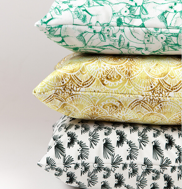 Pillows in Celosia Velvet Image of 3 stacked pillows in Celosia velvet. Designs include green and white deer, gold and white art deco design and black and white hedgehog doodle.