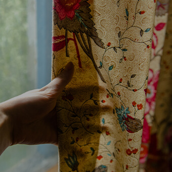 A hand behind beige and warm toned floral printed curtains